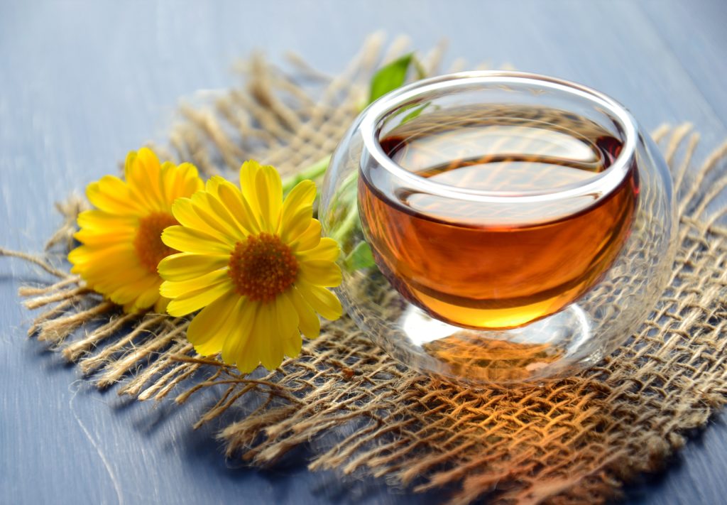 Glass of herbal tea with yellow flowers laying next to it