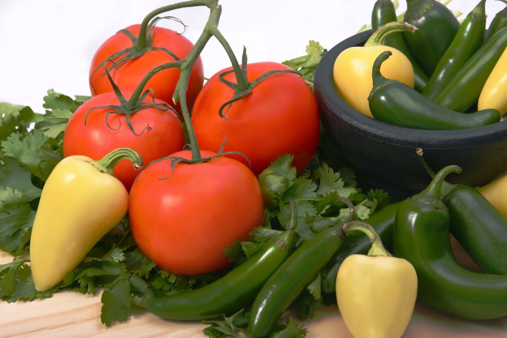 Vine grown tomatoes on a bed of cilantro along with yellow and green chilies.