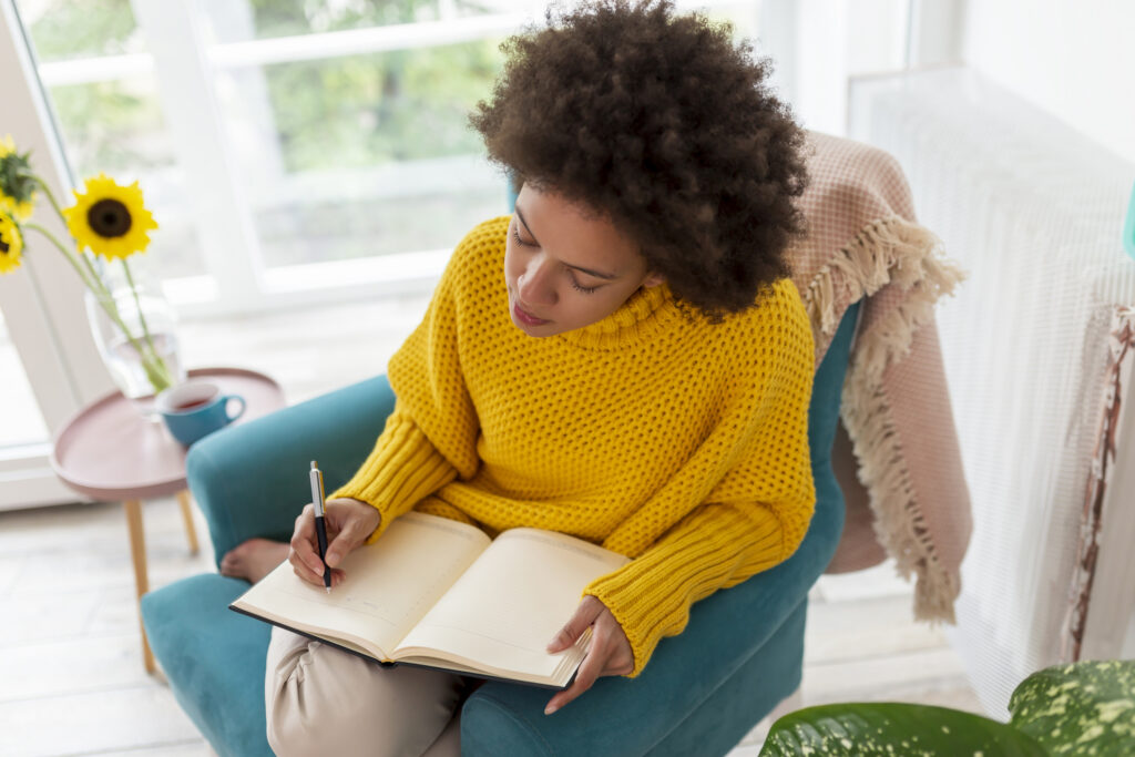 Portrait of a beautiful mixed race woman sitting in an armchair, making a schedule and writing in a planner