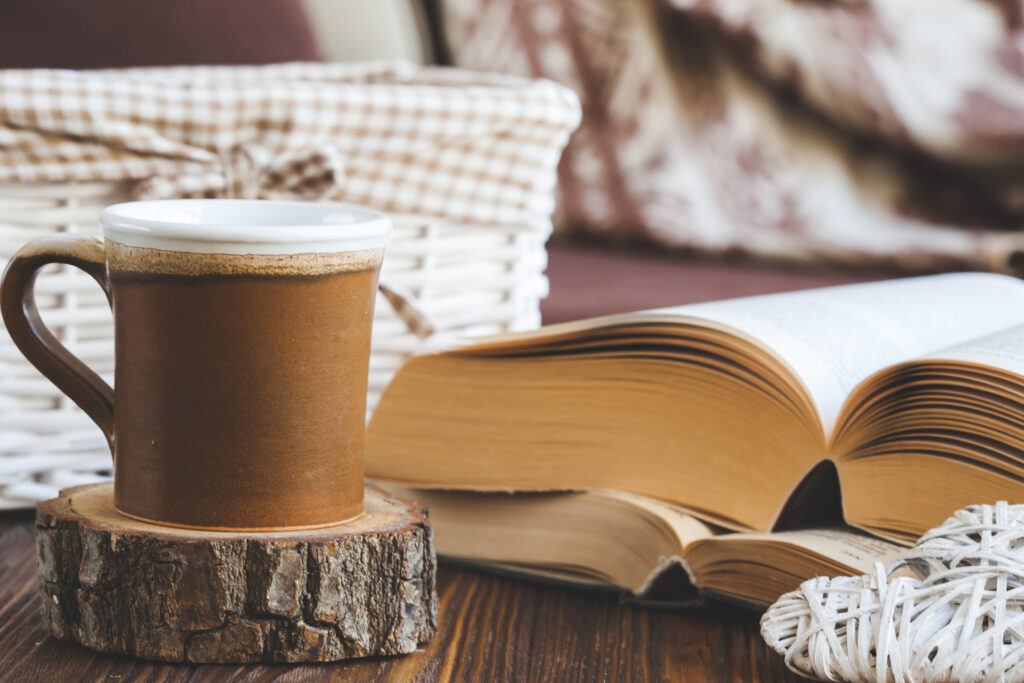 Details of still life in the home interior living room. Beautiful tea cup, cut wood, books and pillows, candle on wooden background. Vintage, rustic. Cozy autumn-winter concept