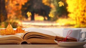 View of leaving falling outside. Beautiful tea cup with tied cinnamon sticks, dried and colorful leaf, and books. Cozy autumn concept