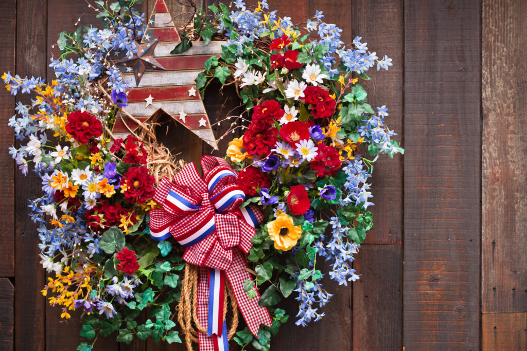 A close up of an Fourth of July wreath hanging on a wood fence.