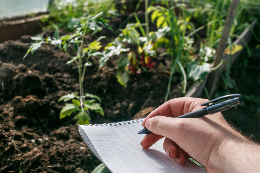 Closeup of a hand holding a pen writing on a notebook overlooking a garden