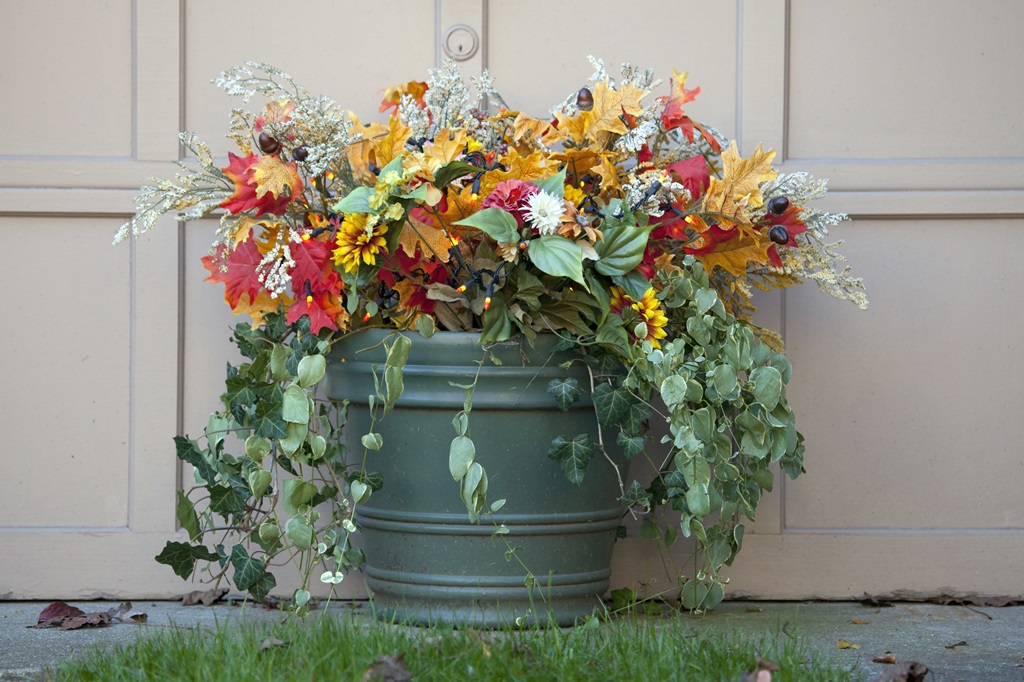 Decoration of autumnal flowers and leaves in a pot in front of a beige garage door