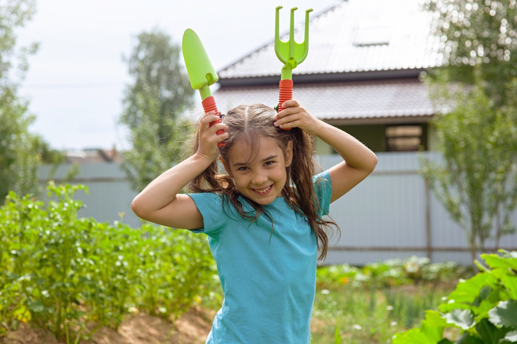 Funny little girl holding small gardening tools , standing in the garden