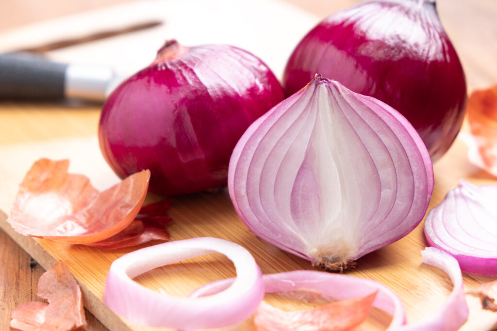 Red Onion and sliced onion on wooden cutting board.
