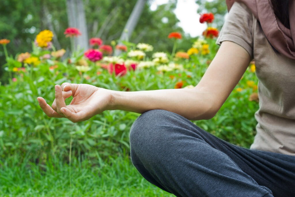 A woman meditating outdoors in a flower garden