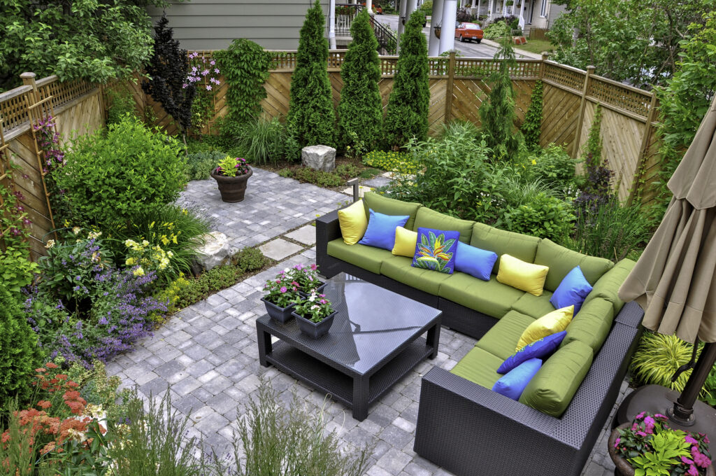 A beautiful small, urban backyard garden featuring a tumbled paver patio, flagstone stepping stones, and a variety of trees, shrubs and perennials add colour and year round interest.